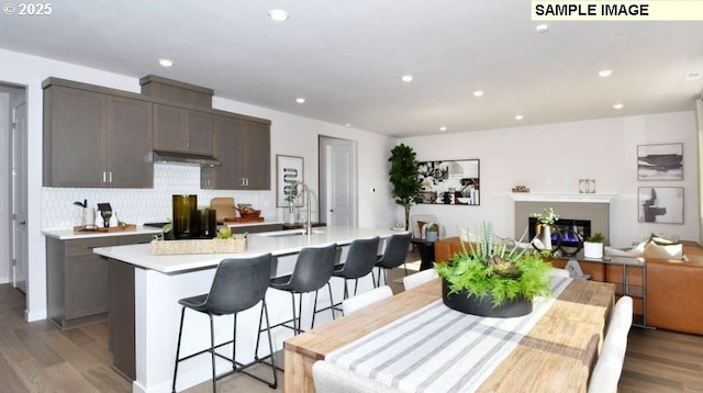 kitchen with a center island with sink, a kitchen bar, light wood-type flooring, backsplash, and sink