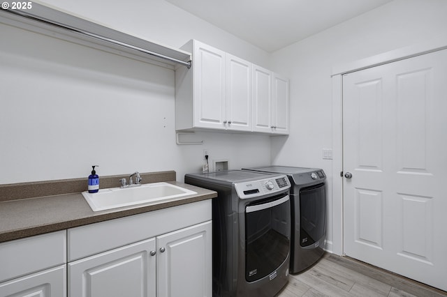 laundry area featuring washing machine and dryer, cabinet space, a sink, and light wood finished floors