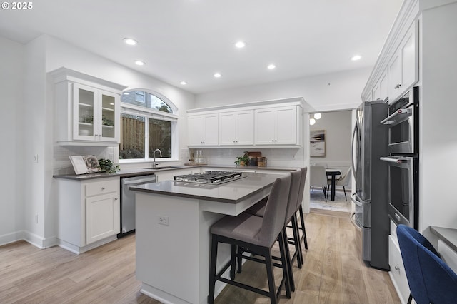 kitchen featuring appliances with stainless steel finishes, white cabinets, light wood-style floors, and a kitchen bar