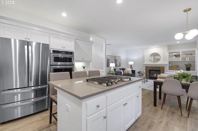 kitchen with a kitchen island, appliances with stainless steel finishes, light wood-style floors, a fireplace, and white cabinetry