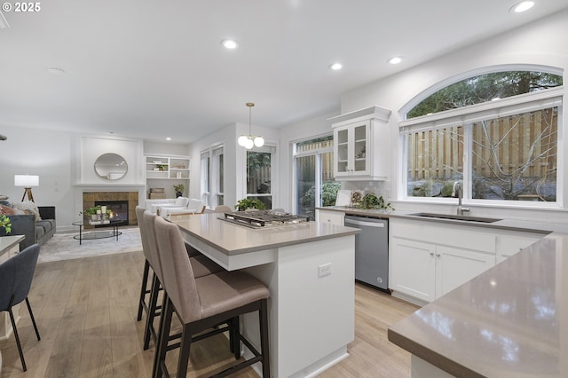 kitchen featuring stainless steel appliances, white cabinets, a sink, a kitchen island, and a tile fireplace