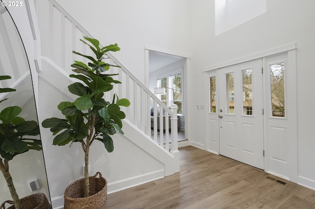 foyer with visible vents, a towering ceiling, light wood finished floors, and stairs