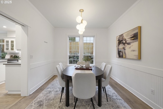 dining space with a wainscoted wall, ornamental molding, and light wood-type flooring