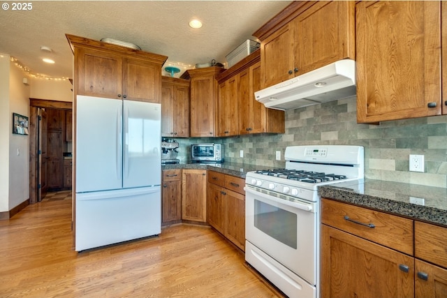 kitchen featuring white appliances, under cabinet range hood, brown cabinets, decorative backsplash, and light wood-style floors