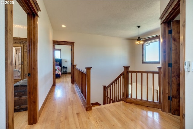 hall featuring an upstairs landing, light wood finished floors, recessed lighting, and baseboards