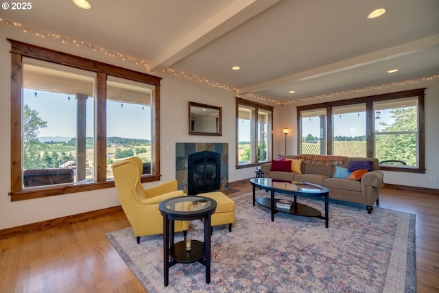 living room featuring baseboards, wood finished floors, a tiled fireplace, recessed lighting, and beamed ceiling