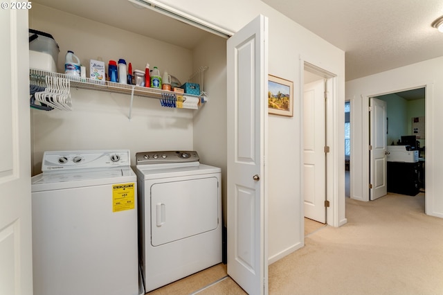 laundry room featuring light colored carpet, a textured ceiling, and washer and clothes dryer