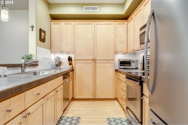 kitchen featuring light brown cabinetry, sink, decorative light fixtures, light wood-type flooring, and appliances with stainless steel finishes