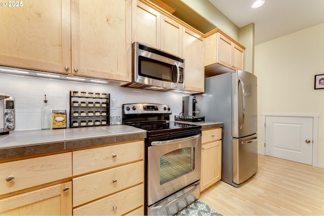 kitchen featuring tasteful backsplash, tile countertops, light brown cabinets, stainless steel appliances, and light hardwood / wood-style floors