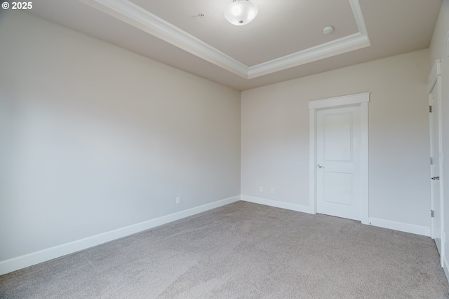 carpeted empty room with ornamental molding, a tray ceiling, and baseboards