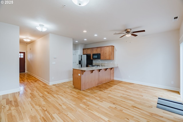 kitchen with a peninsula, visible vents, a kitchen breakfast bar, black appliances, and light wood finished floors