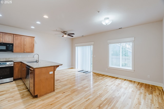 kitchen featuring light stone counters, appliances with stainless steel finishes, a sink, light wood-type flooring, and a peninsula