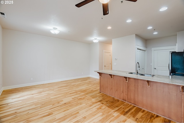 kitchen with light stone counters, a breakfast bar, refrigerator, light wood-style flooring, and a sink