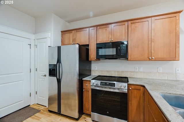 kitchen with brown cabinets, light wood finished floors, appliances with stainless steel finishes, a sink, and light stone countertops