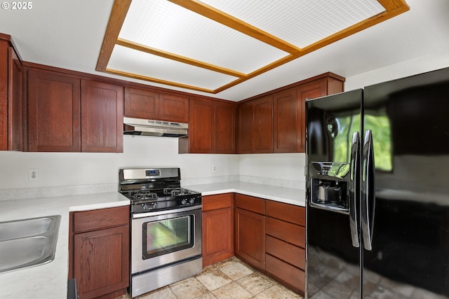 kitchen featuring stainless steel gas stove, black fridge, under cabinet range hood, light countertops, and a sink