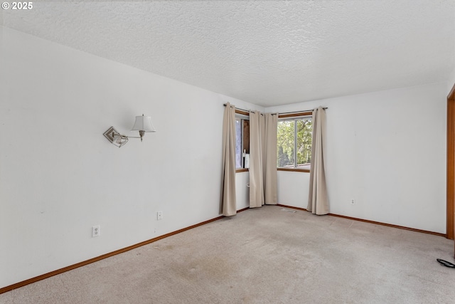 spare room with a textured ceiling, light colored carpet, and baseboards
