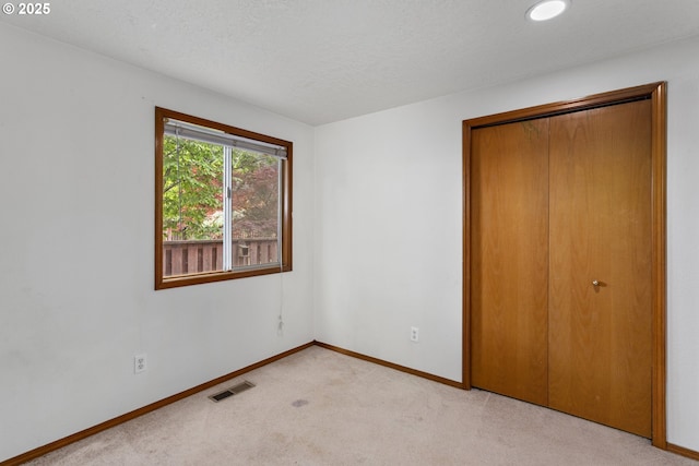 unfurnished bedroom featuring light carpet, baseboards, a closet, and a textured ceiling