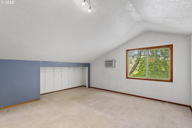 bonus room featuring a textured ceiling, lofted ceiling, a wall mounted air conditioner, carpet, and baseboards