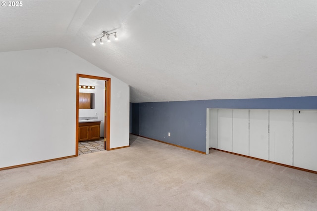 bonus room featuring lofted ceiling, light colored carpet, baseboards, and a textured ceiling