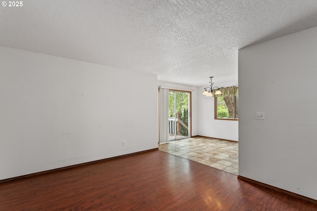empty room with a chandelier, a textured ceiling, wood finished floors, and baseboards