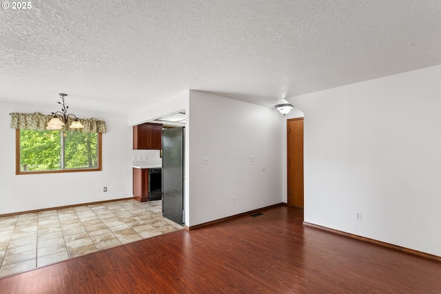 unfurnished living room with a chandelier, light wood finished floors, a textured ceiling, and baseboards
