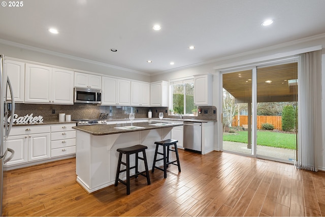 kitchen featuring a kitchen island, a breakfast bar area, white cabinets, appliances with stainless steel finishes, and dark stone countertops