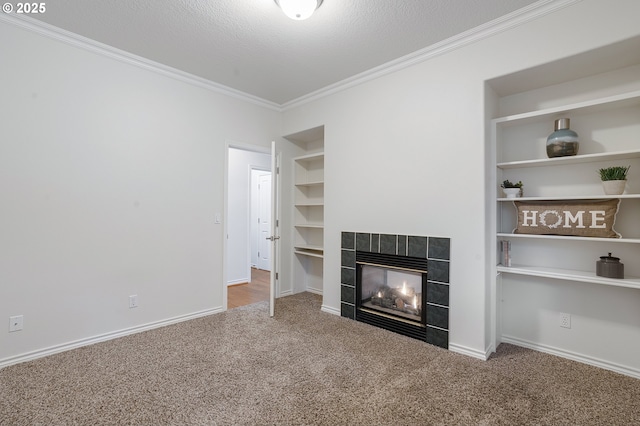 unfurnished living room featuring a tile fireplace, a textured ceiling, carpet, ornamental molding, and built in shelves