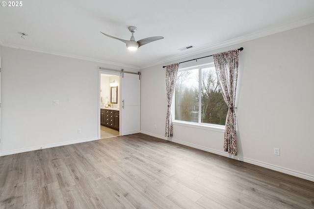 interior space with ornamental molding, ceiling fan, light wood-type flooring, a barn door, and ensuite bath