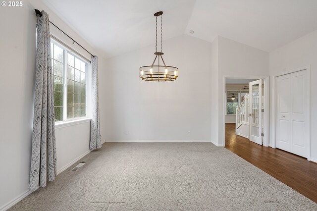 carpeted spare room featuring a notable chandelier and lofted ceiling