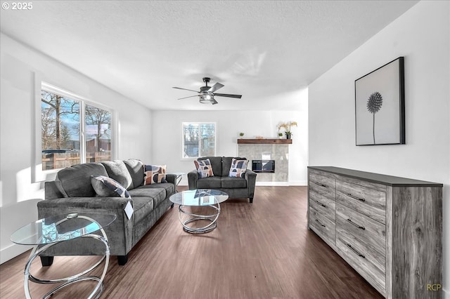 living room with ceiling fan, a wealth of natural light, dark hardwood / wood-style flooring, and a fireplace