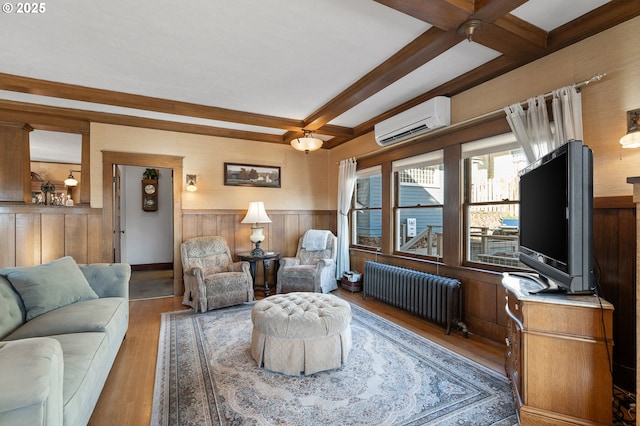 living area featuring radiator, wainscoting, wood finished floors, a wall mounted air conditioner, and beamed ceiling