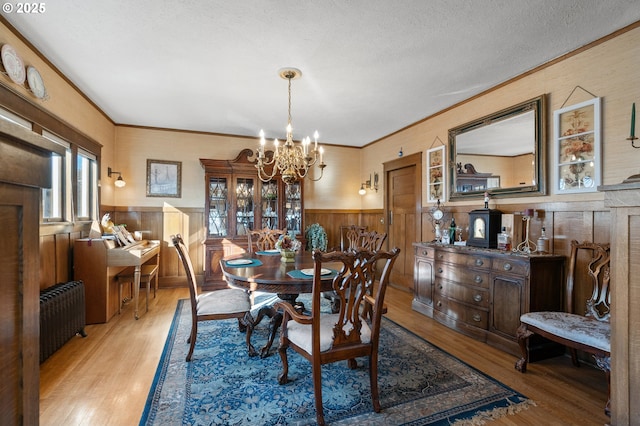 dining area with radiator, a wainscoted wall, crown molding, and wood finished floors