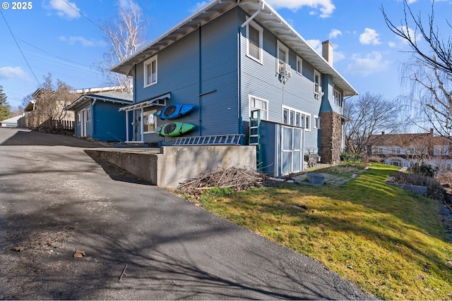 view of property exterior with a chimney, aphalt driveway, and a yard