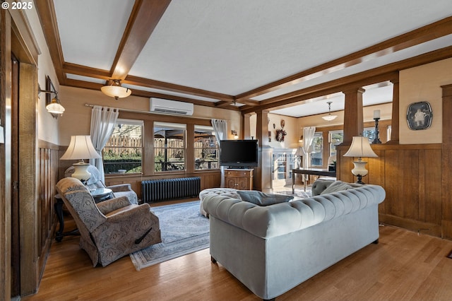 living area featuring a wall unit AC, radiator heating unit, beam ceiling, and wood finished floors