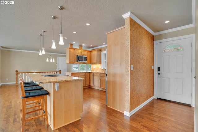 11675 SW Lynn St, Portland, OR 97223 - kitchen with stainless steel microwave, ornamental molding, wood finished floors, light brown cabinets, and a kitchen island