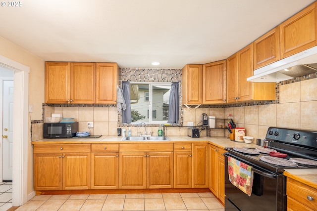 kitchen with light tile patterned flooring, under cabinet range hood, a sink, black appliances, and tasteful backsplash