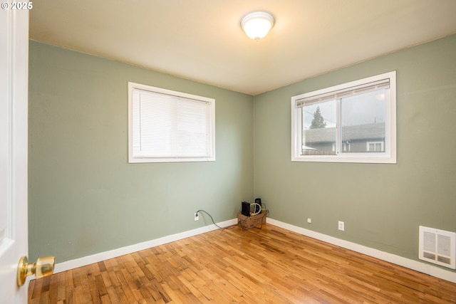 spare room featuring hardwood / wood-style flooring, visible vents, and baseboards