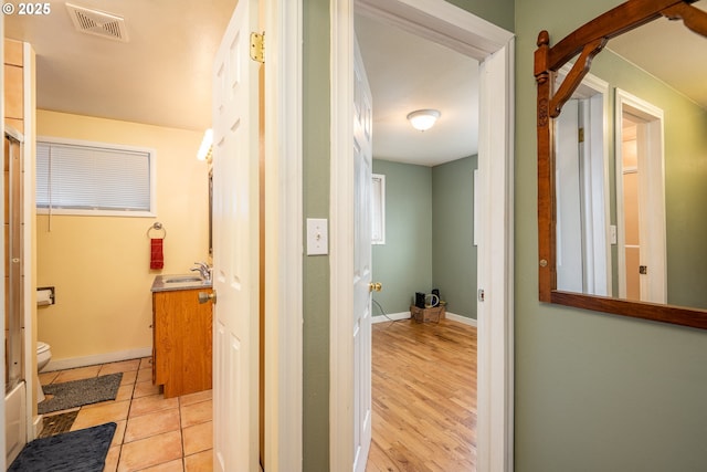 hall with light tile patterned floors, baseboards, and visible vents