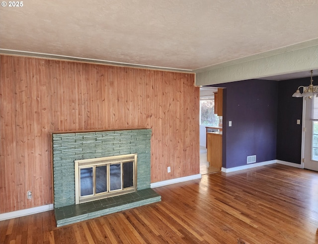 unfurnished living room with visible vents, a notable chandelier, wood finished floors, baseboards, and a brick fireplace