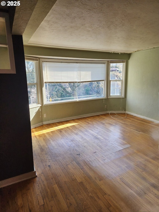 empty room with hardwood / wood-style flooring, baseboards, and a textured ceiling