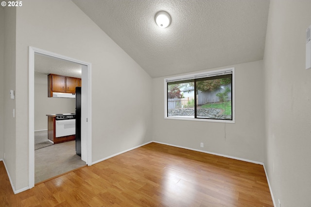 spare room featuring light wood-type flooring, a textured ceiling, lofted ceiling, and baseboards