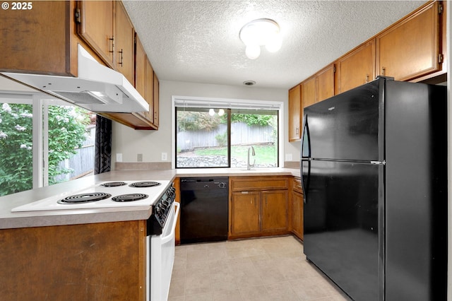 kitchen with brown cabinetry, light countertops, a textured ceiling, under cabinet range hood, and black appliances