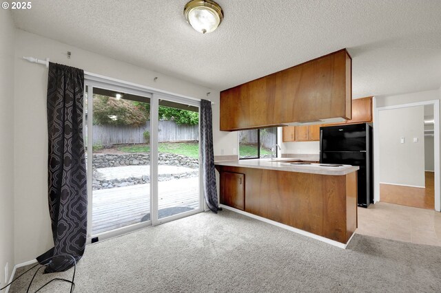 kitchen with freestanding refrigerator, a peninsula, a textured ceiling, and light carpet