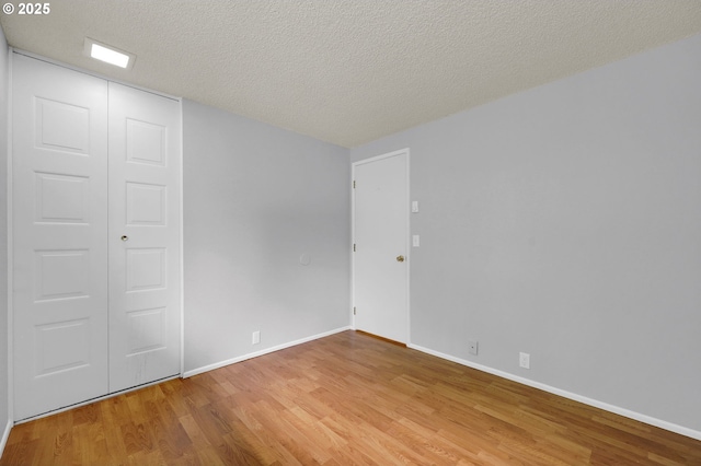 empty room featuring baseboards, light wood-type flooring, and a textured ceiling