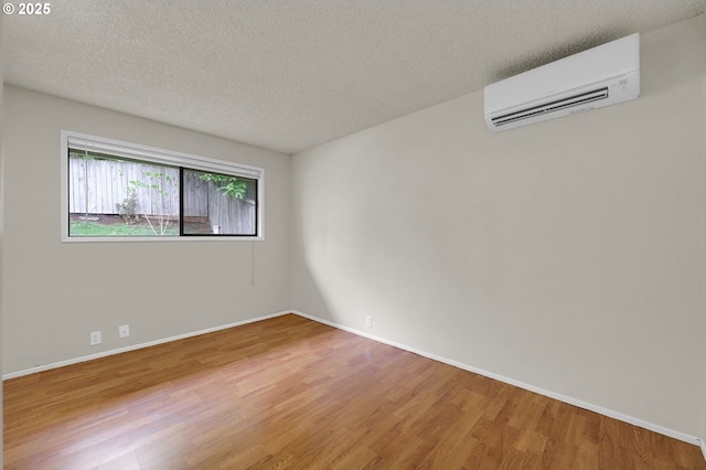 spare room featuring a textured ceiling, baseboards, a wall unit AC, and wood finished floors