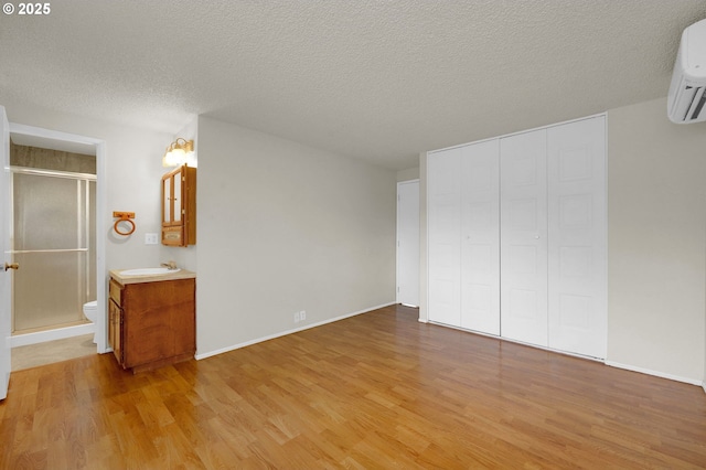 unfurnished bedroom featuring a sink, light wood-style floors, an AC wall unit, a textured ceiling, and a closet