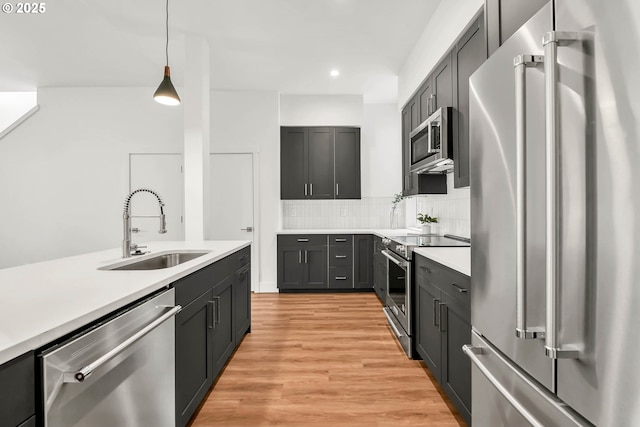 kitchen with sink, decorative light fixtures, decorative backsplash, appliances with stainless steel finishes, and light wood-type flooring