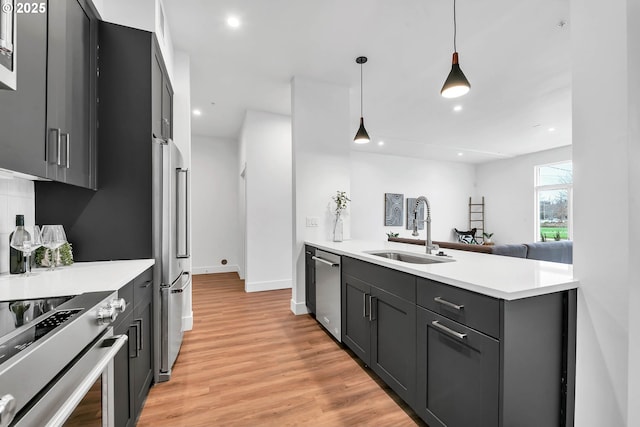 kitchen featuring pendant lighting, high quality appliances, sink, and light hardwood / wood-style flooring