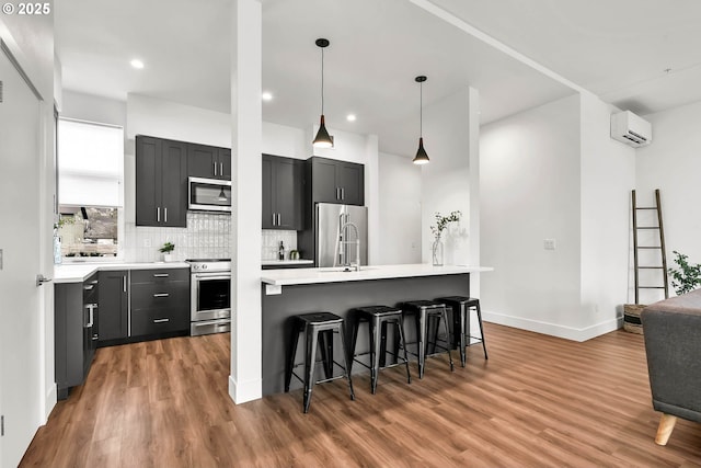 kitchen featuring a center island, a kitchen breakfast bar, a wall mounted AC, decorative light fixtures, and stainless steel appliances