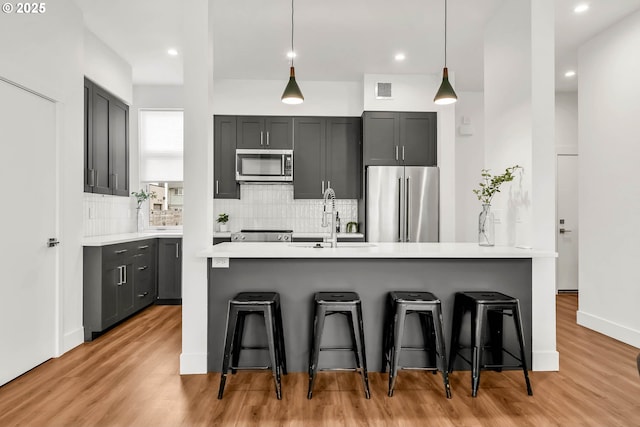 kitchen with a breakfast bar, light wood-type flooring, decorative light fixtures, and appliances with stainless steel finishes